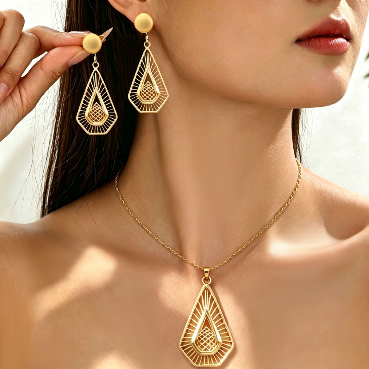 Model wearing gold-tone teardrop openwork earrings with a coordinating pendant necklace